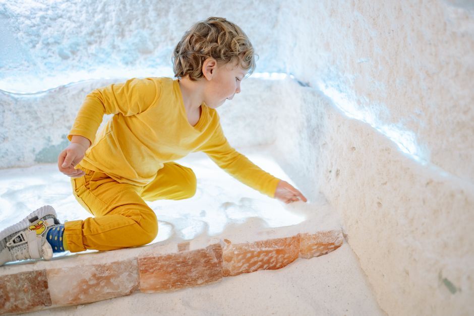 Young boy in a yellow outfit climbing on brick steps inside a pale, rocky grotto.